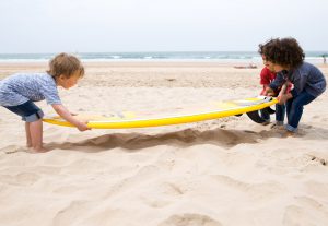 children carrying a surf board